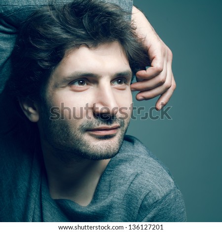 Portrait of happy fashionable handsome mature man in gray sweater (pullover) posing over dark blue (green) background with a friendly smile. Hand on head. Perfect hair and skin. Close up. Studio shot