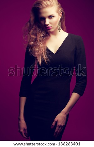 Portrait of a red-haired (ginger) fashionable model in a black classic cocktail dress posing over purple background. Seductive glance. Vogue style. Studio shot