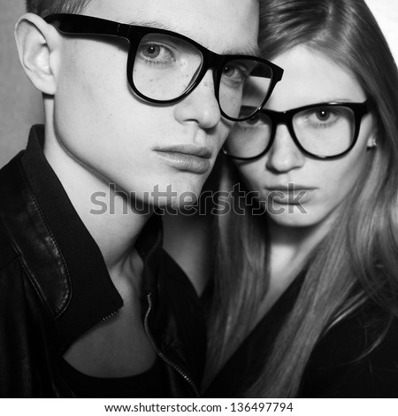 Family Portrait Of Gorgeous Blond Fashion Twins In Black Clothes Wearing Trendy Glasses And Posing Over Gray Background Together. Perfect Hair. Natural Make-Up. Perfect Skin. Vogue Style. Close Up.