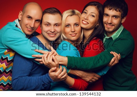 Portrait of five stylish close friends hugging, smiling and posing over red background. Guys having fun. Hipster style. Studio shot