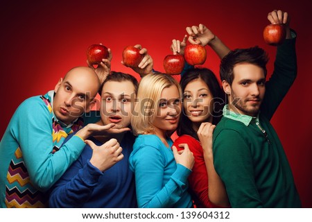 Portrait of funny and confused students (close friends) posing over red background and holding red apples above heads. Education (health-care) concept. Hipster style. Studio shot