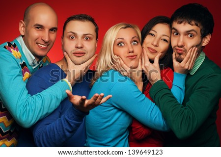 Portrait of five stylish close friends hugging, smiling and posing over red background. Guys having fun and holding cheeks of their neighbor. Hipster style. Studio shot
