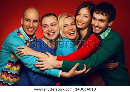 Portrait of five stylish close friends hugging and posing over red background. Guys having fun. Shiny smile and healthy white teeth. Hipster style. Studio shot