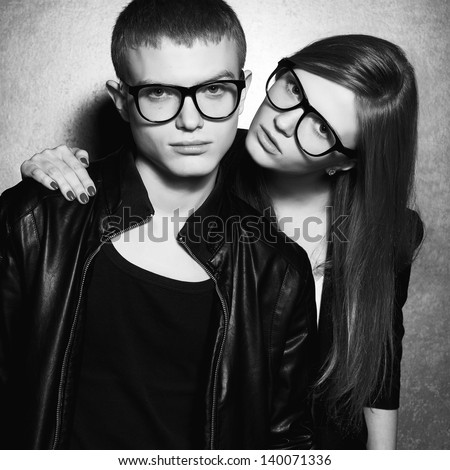 Portrait of gorgeous fashion twins in black clothes wearing trendy glasses and posing over metal background together. Perfect hair and skin. Natural make-up. Black and white studio shot