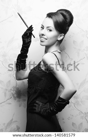 Retro portrait of a beautiful woman in great cocktail dress smoking a cigarette with holder. Jewelry and Beauty. Vintage (Hollywood) style. Classic old movie star. Black and white studio shot