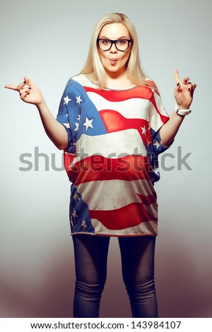 American Dream (Lifestyle) Concept: Young pregnant woman in american flag like dress and trendy glasses dancing over gray background with a fish face emotion (kiss). Hipster style. Studio shot