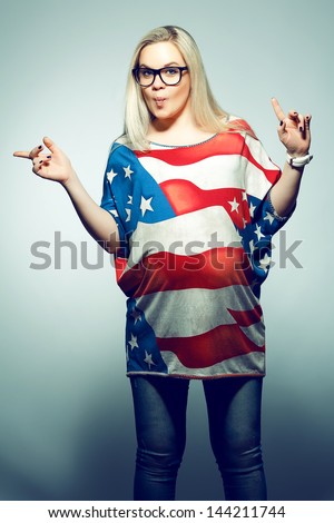 American Dream (Lifestyle) Concept: Young pregnant woman in american flag like dress and trendy glasses dancing over gray background with a fish face emotion (kiss). Hipster style. Studio shot