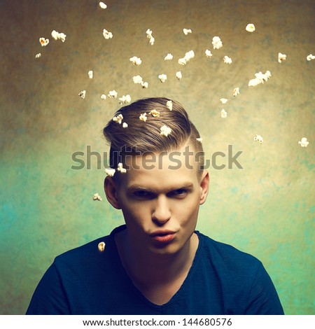 Unhealthy eating. Junk food concept. Portrait of fashionable young man making popcorn flying over golden background. Great haircut and healthy skin. Disgusted expression on face. Studio shot