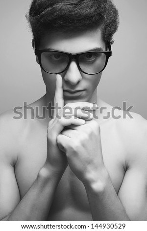 Eyewear concept. Handsome muscular male model with nice body wearing trendy glasses, thinking something about and posing over gray background. Boy looks like cute maniac. Hipster style. Close up
