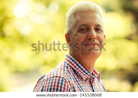 Portrait of a smiling happy mature (old) man in trendy casual shirt posing in the park. Sunny summer day. Copy-space. Close up. Outdoor shot