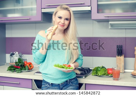 Healthy pregnancy concept. Portrait of a lovely young pregnant woman enjoying fresh food (bread and salad)  in her modern hi-tech kitchen. Trendy clothing on girl. Indoor shot
