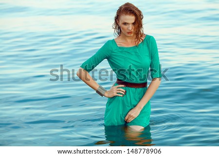Fashion portrait of a young model with wet long ginger (red) hair in blue dress posing at the seaside. Perfect skin and make-up. Copy-space. Outdoor shot