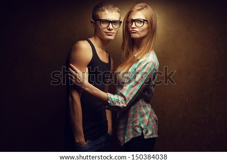 Portrait of gorgeous red-haired (ginger) fashion twins in casual shirts wearing trendy glasses and posing over golden background together. Sister touching brother\'s bicep. Hipster style. Studio shot