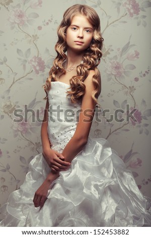 Portrait of a little princess in white vapory classic dress with pearls posing over vintage background. Perfect glossy long hair. Retro & Vogue style. Studio shot