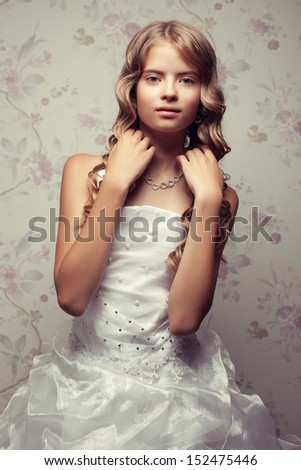 Portrait of a little princess in white vapory classic dress with pearls posing over vintage background. Girl touching her perfect glossy long hair. Retro & Vogue style. Studio shot