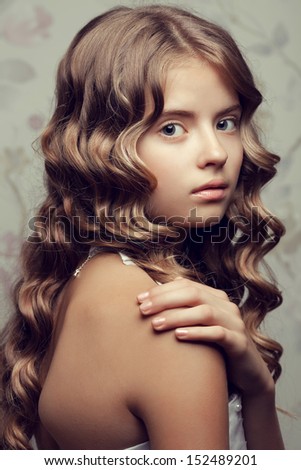 Portrait of a little princess in white classic dress with pearls posing over vintage background. Girl with perfect glossy long hair touching her shoulder. Retro & Vogue style. Close up. Studio shot