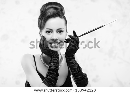 Retro movie star concept. Portrait of beautiful actress in a great black cocktail dress smoking a cigarette with holder. Perfect shiny smile & skin. Vintage (old Hollywood) style. Close up. Copy-space