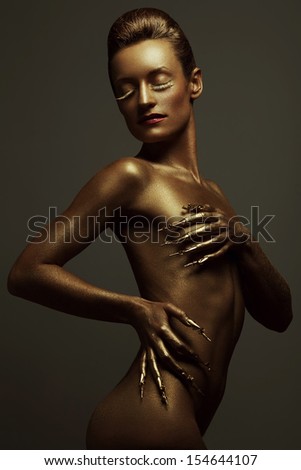 Golden statue of Valkyrie concept. Arty portrait of model with golden healthy skin and shiny lashes. Perfect sporty body. Golden long nails. Studio shot