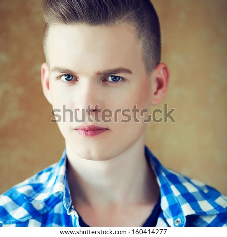 Portrait of a young man with very handsome face in blue casual shirt with stylish haircut posing over golden brown background. Perfect skin and haircut. Hipster style. Close up. Studio shot