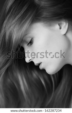 Profile portrait of a beautiful girl with freckles on her face. Healthy long and wavy hair. Daylight. Close up. Black and white (monochrome) studio shot