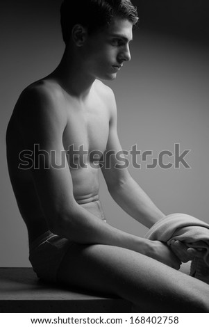Male high fashion concept. Portrait of a handsome male model sitting on a wooden cube in stylish underwear. Perfect skin & haircut. Vogue style. Profile. Copy-space. Black and white studio shot