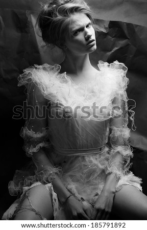 Emotive retro portrait of a crazy queen like girl posing in white wedding dress over wrinkled black paper background. Vintage style. Black and white (monochrome) studio shot