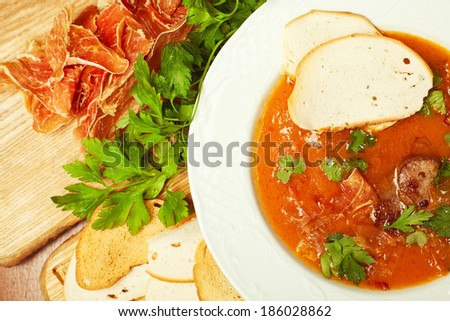 Tomato soup with smoked bacon and fresh parsley on a wooden board with dry toasts. Close up. Indoor shot