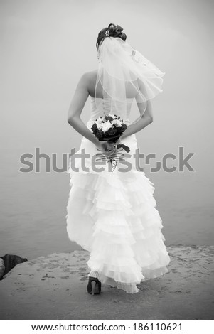 Portrait of a bride with a wedding bouquet on the coast of the sea. Outdoor black and white shot