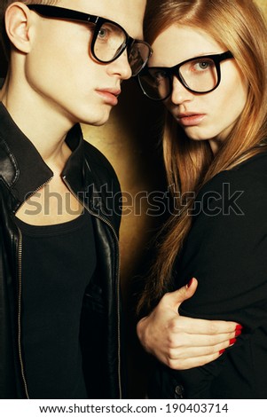 Eyewear concept. Family portrait of gorgeous blond fashion twins in black clothes wearing trendy glasses and posing over golden background together. Perfect skin. Vogue style. Studio shot