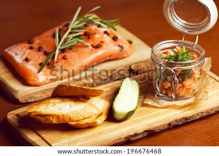 Mason jar with pieces of salmon with fresh cucumber, toasts and ruccola and served with parchment paper on wooden board in restaurant. Vintage style. Close up