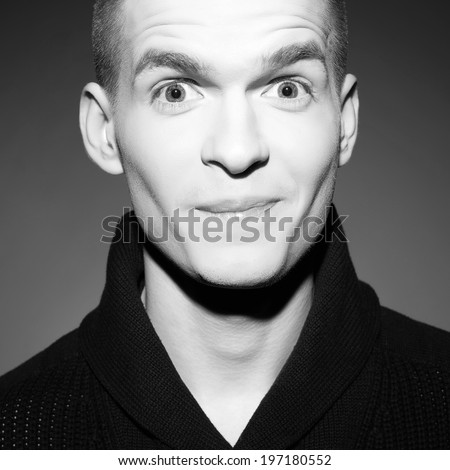 Wow face concept. Fashion portrait of a smiling elegant young and handsome man posing over dark gray background. Wondered emotive face. Close up. Black and white studio shot