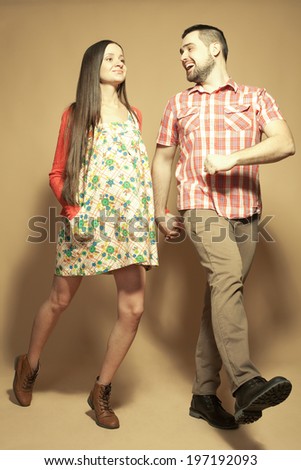 Stylish pregnancy concept: portrait of two happy hipsters (husband and wife) expecting their child and walking in trendy clothes (shirt, dress, cardigan, jeans and leather boots). Studio shot