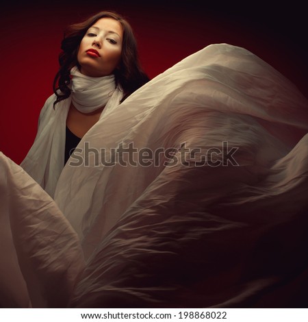 Arty portrait of beautiful brunette with great make-up and flying vapory white silk scarf looking like white cloud. Fashion girl posing over dark red background. Vogue style. Studio shot