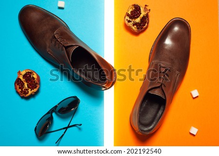 Stylish and arty hipster fashion concept in avant-garde style. Trendy eyewear and leather shoes on blue and orange background with pomegranates, sugar cubes and white neon lamp. Studio shot