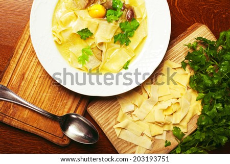 Chicken soup with pasta (noodle) with fresh parsley in white porcelain plate on a wooden board with metal spoon in european cafe. Close up. Indoor shot