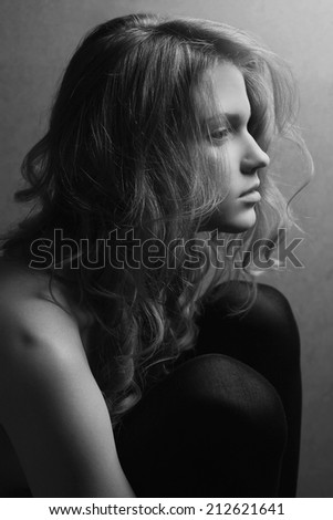 Emotive portrait of a young beautiful girl with long hair in profile hugging her knees and posing over gray background. Close up. Studio shot