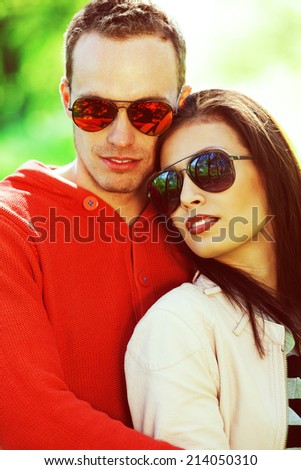Eyewear concept. Smiling young woman and her boyfriend in trendy sunglasses posing in the park. Stylish casual clothing. White shiny smiles. Spring (autumn) sunny weather. Close up. Outdoor shot