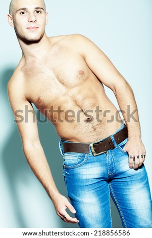 Tough guy concept. Emotive portrait of handsome young man looking at camera with arms in pockets of blue jeans, posing over blue background. Great muscles and healthy skin. Urban style. Studio shot