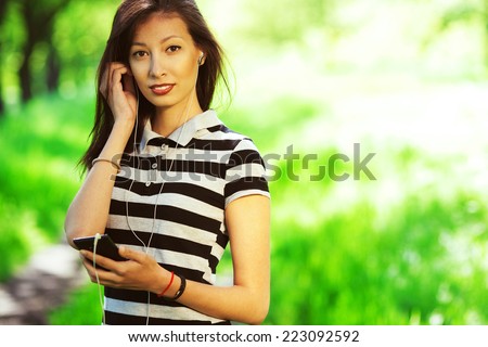 Happy weekend concept. Portrait of a beautiful girl in casual t-shirt using her smartphone in park. Sunny summer (autumn) weather. Close up. Hipster style. Copy-space. Outdoor shot