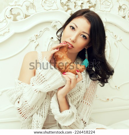 Perfect wake up concept. Portrait of young beautiful woman having breakfast (eating croissant) in vintage bedroom. Retro (classic) style. Close up. Indoor shot