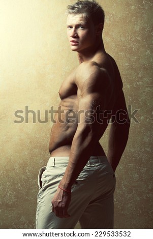 Male beauty & fashion concept. Portrait of handsome muscular male model in trendy summer pants posing over golden background. Blond hair and healthy clean skin. Studio shot