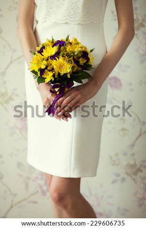 Bride\'s hands with wedding bouquet of violet and yellow flowers over stylish white dress. Vintage style. Close up. Indoor shot