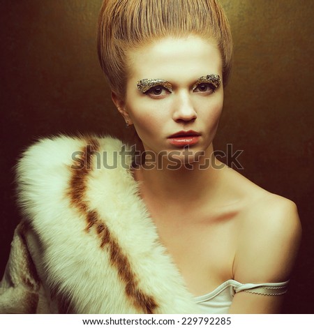 Venus in furs concept. Portrait of fashionable red-haired model with perfect arty make-up, vintage hairdo wearing luxury fur coat and posing over golden background. Retro style. Close up. Studio shot
