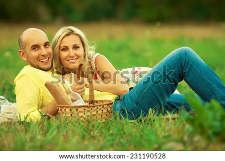 Happy moments of new family concept. Portrait of beautiful young couple having picnic in countryside. Smiling man and woman in trendy casual clothing with italian wine & bread in basket. Outdoor shot