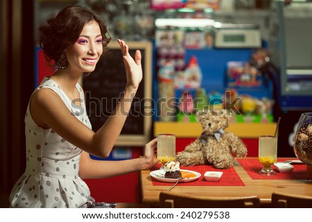 Welcome concept. Portrait of doll like brunette girl with retro hairdo in white trendy vintage polka-dot sleeveless dress drinking tea, saying hello. Close up. Copy-space. Indoor shot