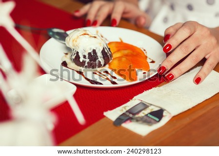 Haute cuisine concept. Woman\'s hands with perfect manicure and ice cream brownie sundae with chocolate sauce and slices of date plum on white plate. Close up. Indoor shot