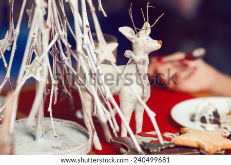Christmas decoration concept. Vintage toy - christmas deer - with bow on its neck standing over white christmas tree in restaurant. Pastel colors. Retro style. Close up. Indoor shot