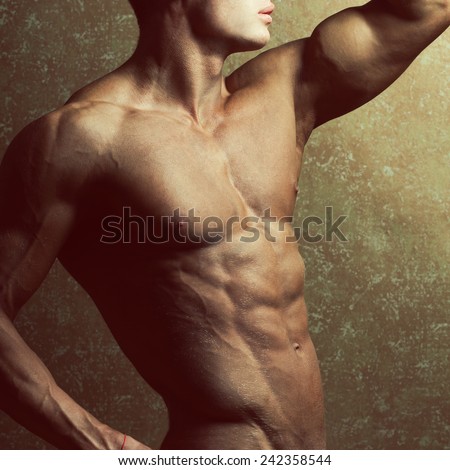 Bodybuilding and body sculpture concept. Beautiful (handsome) muscular male model with perfect body posing over golden background. Close up. Studio shot