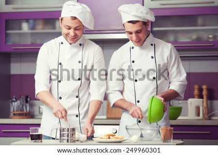 Tiramisu cooking concept. Portrait of two smiling men in cook uniform making italian dessert in modern kitchen. Indoor shot