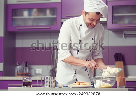 Tiramisu cooking concept. Portrait of smiling man in cook uniform making italian dessert in modern kitchen. Indoor shot